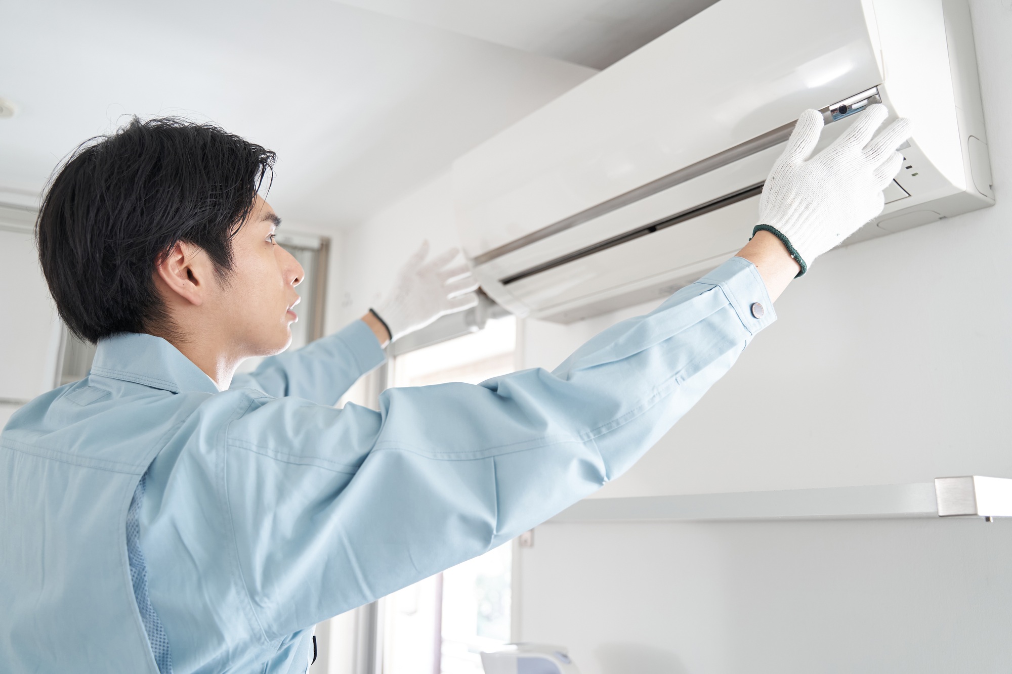 Air conditioning maintenance in Cheverly, Maryland: Technician in gloves inspecting a wall-mounted AC unit for repair and maintenance.