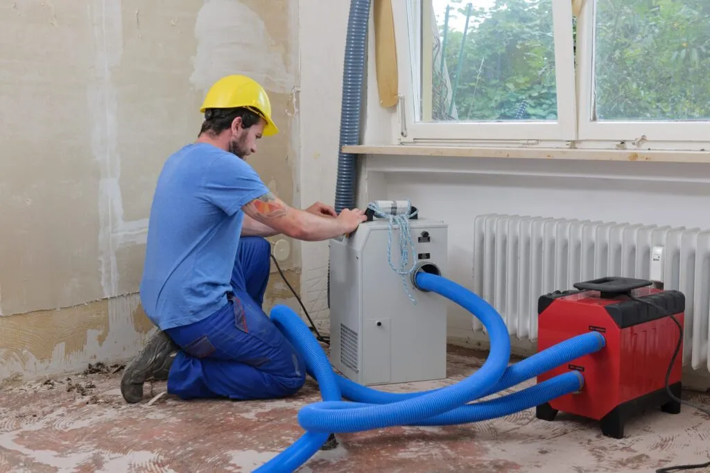 Water damage restoration in Cheverly, Maryland: A technician in a hard hat operates water damage restoration equipment indoors.