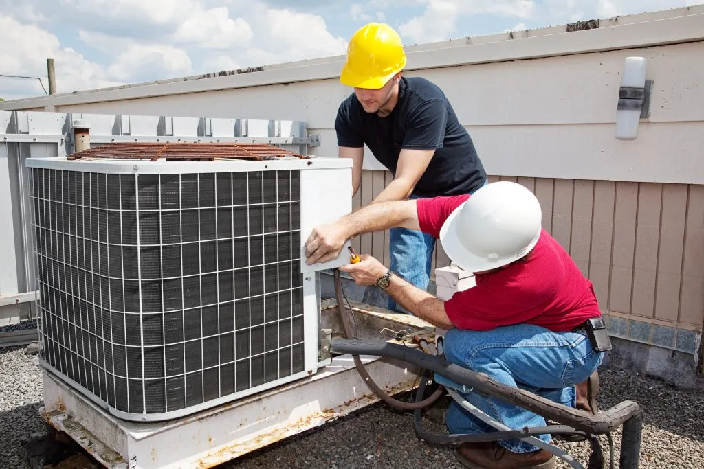 Heating Installation in Cheverly, Maryland: Two technicians in hard hats install a new HVAC system on a commercial rooftop, ensuring efficient heating.