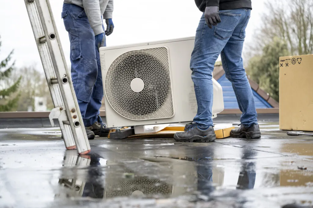 Two workers installing an outdoor unit for an emergency ac system on a wet flat rooftop in Cheverly, Maryland, during the day.